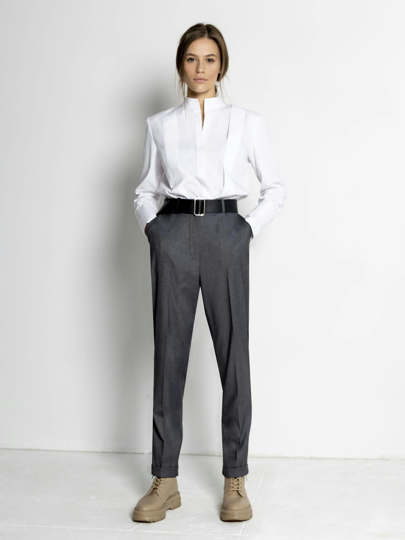 Professional woman in a stylish white blouse and gray trousers fashion pose.
